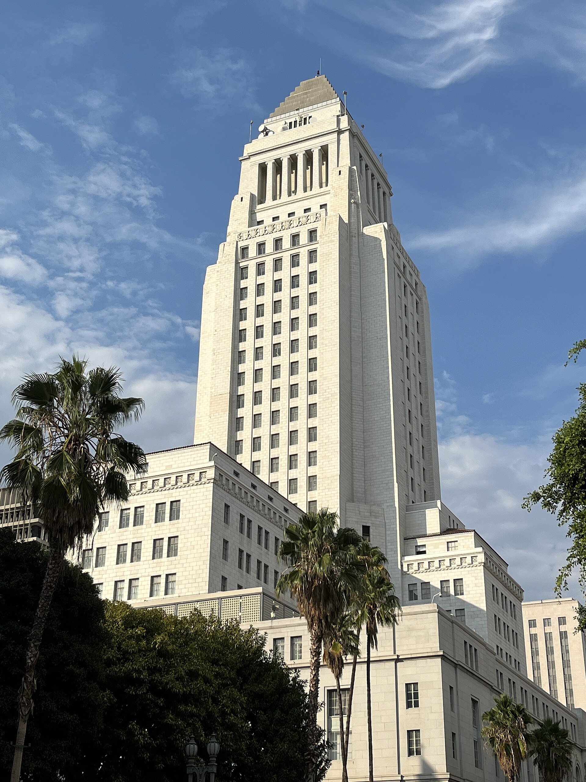 The tower of Los Angeles City Hall rising above palm trees against a blue sky.