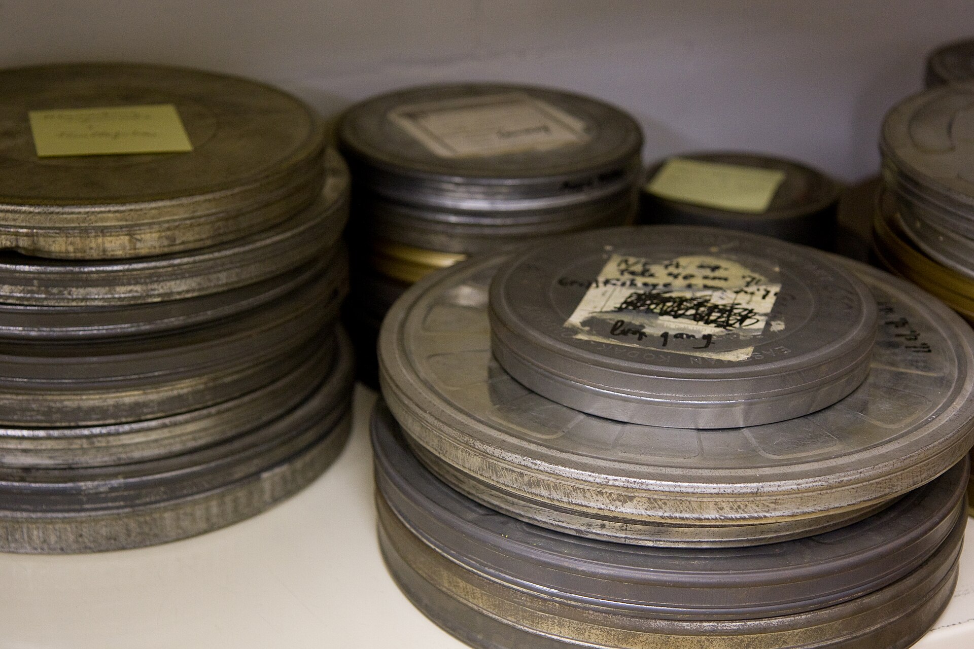 Stacked round metal film cans of various sizes and colors sit on a shelf, their edges labeled and worn.