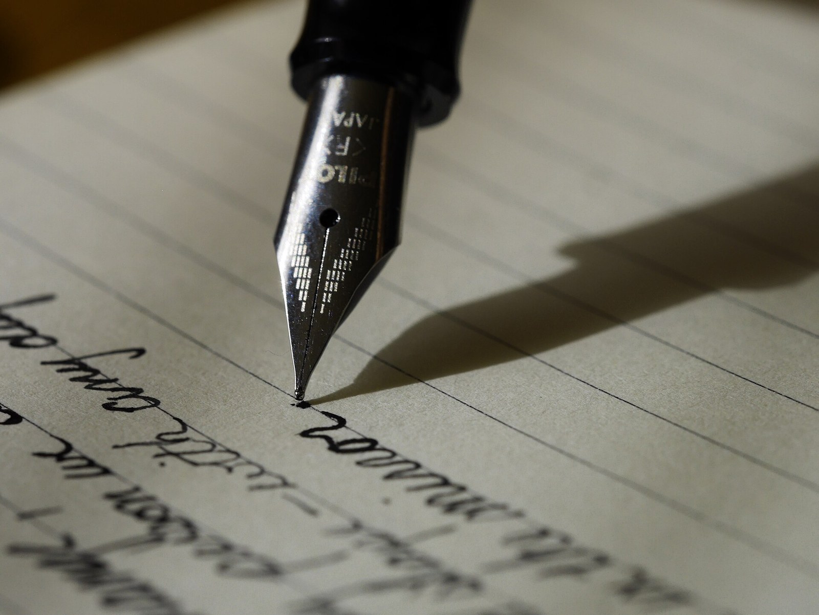 Close-up of a black fountain pen's steel nib touching lined paper, with a few lines of cursive handwriting in black ink below it.