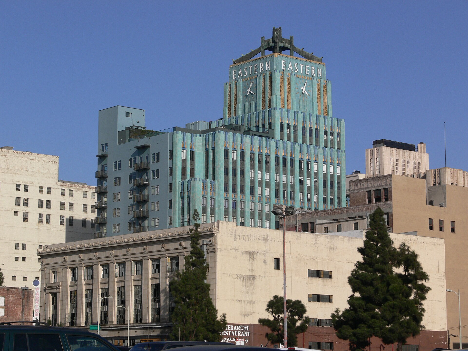 The turquoise terra-cotta tower of the Art Deco Eastern Columbia Building, its clock and "EASTERN" signs at the top, rising above lower downtown buildings against a clear sky.