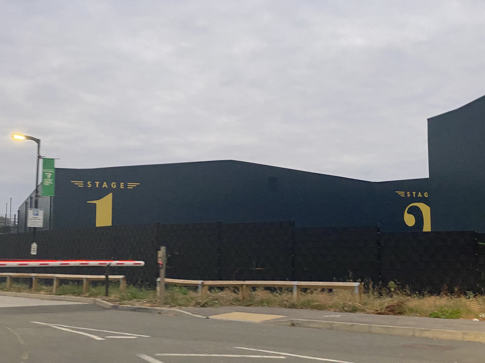The tall charcoal-gray exterior wall of a soundstage marked with a large gold number and the word STAGE, seen from an empty roadway under a flat gray sky.